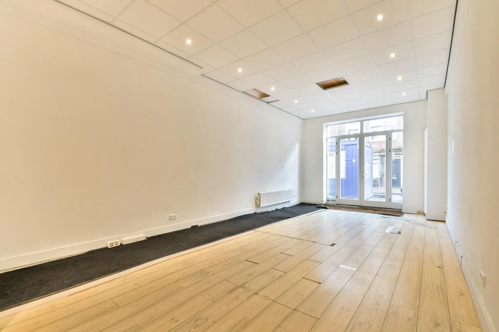 Leegstaand winkelpand aan de Korte Schimmelstraat met houten vloer, systeemplafond en glazen toegangsdeur.